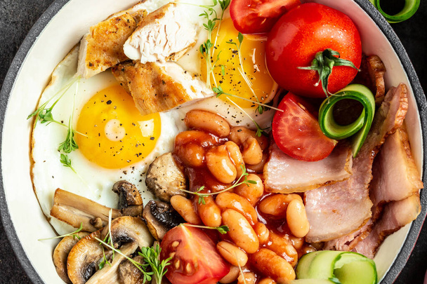 Plná anglická snídaně v pánvi se smaženými vejci, slaninou, fazolemi, tousty a kávou na tmavém pozadí, pohled shora. - Fotografie, Obrázek