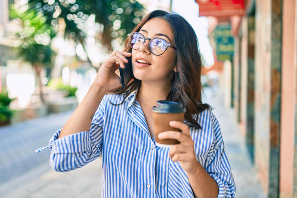 Ciddi bir suratı olan genç İspanyol iş kadını şehirdeki akıllı telefondan konuşuyor.. - Fotoğraf, Görsel