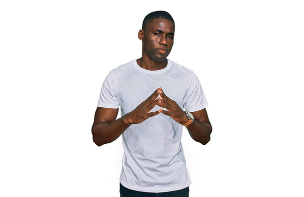Νεαρός Αφροαμερικάνος που φοράει λευκό πουκάμισο με τα χέρια ενωμένα και σταυρωμένα τα δάχτυλα χαμογελώντας χαλαρός και χαρούμενος. επιτυχία και αισιοδοξία  - Φωτογραφία, εικόνα
