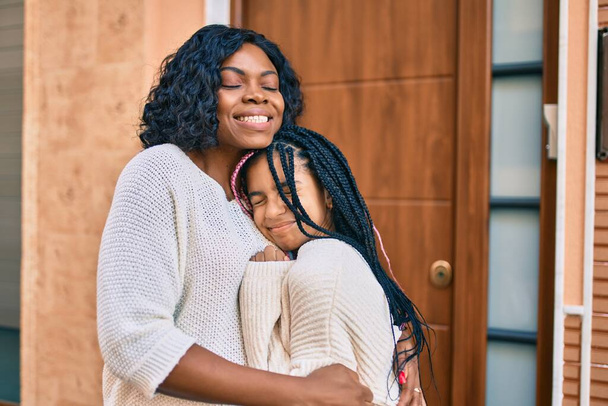 Schöne afrikanisch-amerikanische Mutter und Tochter lächeln glücklich und umarmen sich. Mit einem Lächeln im Gesicht in der Stadt stehen. - Foto, Bild