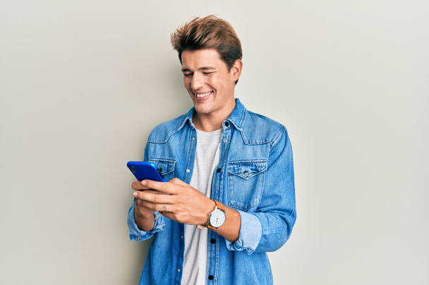 Handsome caucasian man using smartphone smiling with a happy and cool smile on face. showing teeth.  - Photo, Image