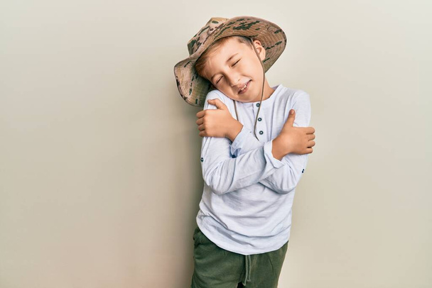 Kleiner kaukasischer Junge mit Forscherhut, der sich glücklich und positiv umarmt und selbstbewusst lächelt. Selbstliebe und Selbstfürsorge  - Foto, Bild