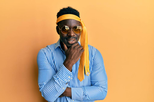 Handsome black man drunk wearing tie over head and sunglasses looking confident at the camera smiling with crossed arms and hand raised on chin. thinking positive.  - Photo, Image