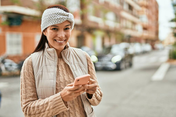 Joven latina sonriendo feliz usando smartphone en la ciudad. - Foto, Imagen