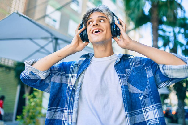 Jovem hispânico sorrindo feliz usando fones de ouvido andando na cidade. - Foto, Imagem