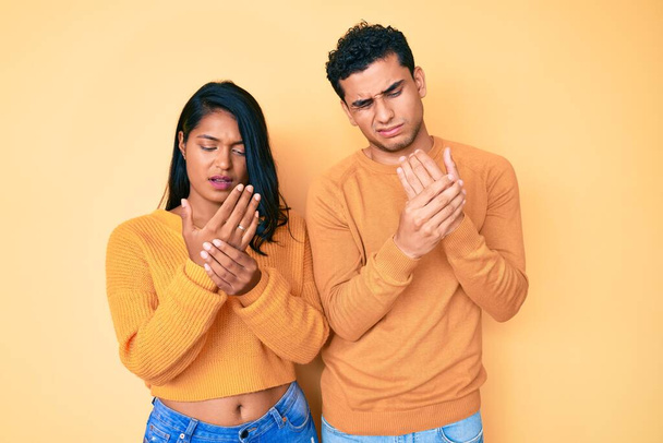 Beautiful latin young couple wearing casual clothes together suffering pain on hands and fingers, arthritis inflammation  - Fotoğraf, Görsel