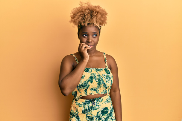 Mujer africana joven con el pelo afro usando vestido de verano buscando estresado y nervioso con las manos en la boca mordiendo las uñas. problema de ansiedad.  - Foto, Imagen