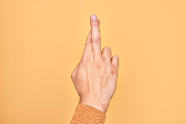 Mano di giovane caucasico che mostra le dita su uno sfondo giallo isolato gesticolando le dita incrociate, superstizione e gesto fortunato, espressione fortunata e di speranza - Foto, immagini