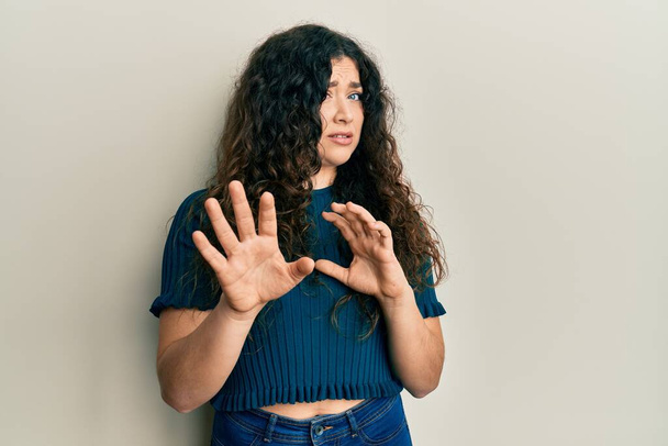 Young brunette woman with curly hair wearing casual clothes disgusted expression, displeased and fearful doing disgust face because aversion reaction. with hands raised  - Photo, Image