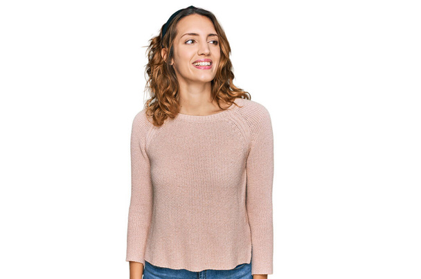Schöne junge kaukasische Frau in lässigem Pullover, die mit einem Lächeln im Gesicht und natürlichem Ausdruck zur Seite schaut. Lachen selbstbewusst.  - Foto, Bild