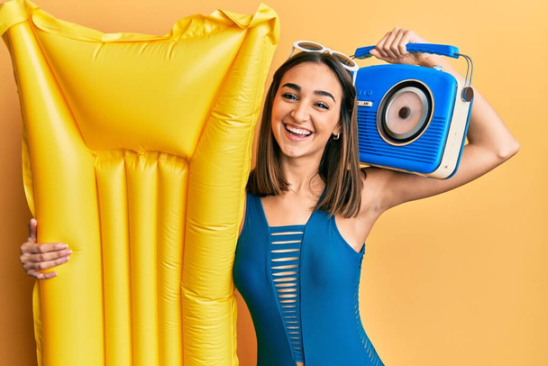 Young brunette girl wearing bikini holding boombox and float smiling and laughing hard out loud because funny crazy joke.  - Foto, afbeelding