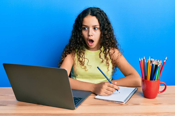 Teenager hispánská dívka sedí na stole studuje do školy strach a šokován s překvapením a užaslý výraz, strach a vzrušený obličej.  - Fotografie, Obrázek
