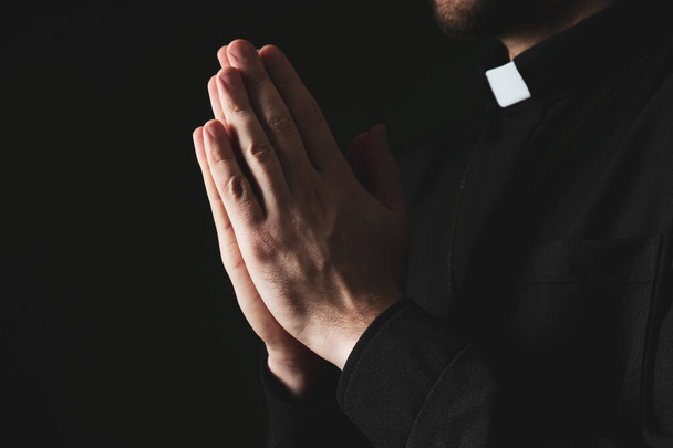 Priest in cassock praying on dark background, closeup - Фото, изображение