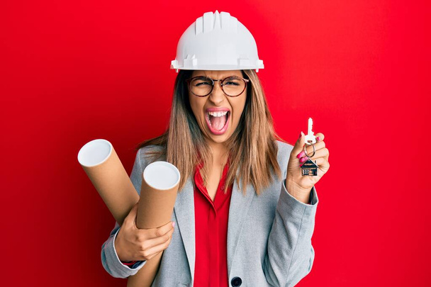 Beautiful brunette woman wearing safety helmet holding blueprints celebrating crazy and amazed for success with open eyes screaming excited.  - Photo, Image
