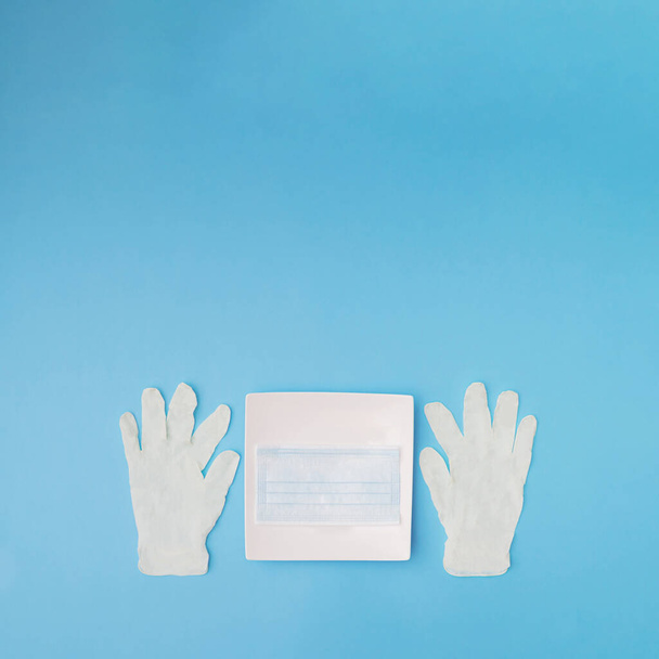 Masque chirurgical bleu dans une assiette avec gants sur fond bleu. Espace de copie. - Photo, image