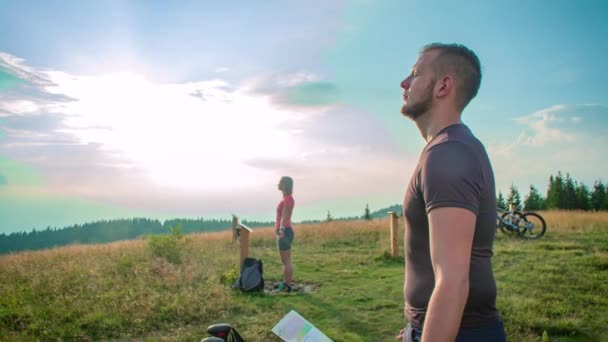 Een man en een vrouw die op een veld voor een bord staan met hun ogen dicht en hun armen open. - Video