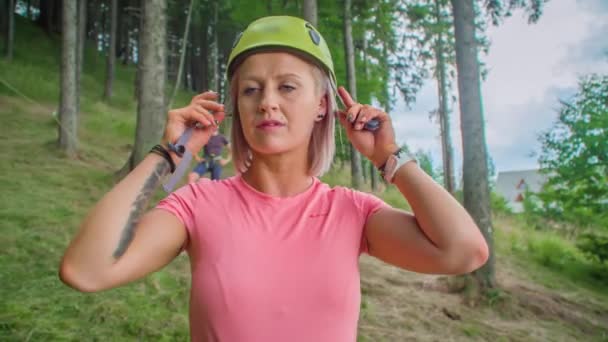 Молодая женщина надевает шлем с мужчиной, ждущим ее в лесу на холме - Кадры, видео