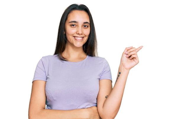 Young hispanic woman wearing casual clothes smiling happy pointing with hand and finger to the side  - Φωτογραφία, εικόνα