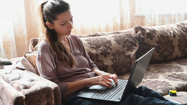 Молодая девушка сидит дома на диване, удаленно работает за компьютером. Высокое качество фото - Фото, изображение