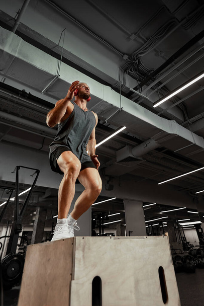 Sexy hombres musculosos utilizando la plataforma para sus piernas en un fondo de color oscuro del gimnasio. - Foto, Imagen