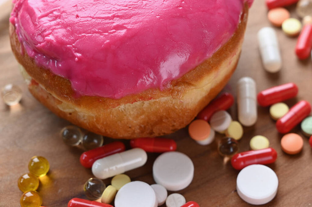 Rosado donut y vitaminas y píldoras multicolores sobre fondo de madera. Medicina y concepto saludable. Foto de alta calidad - Foto, imagen