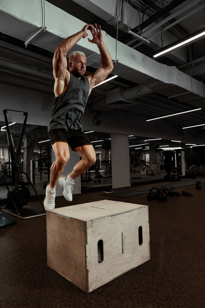 Sexy hombres musculosos utilizando la plataforma para sus piernas en un fondo de color oscuro del gimnasio. - Foto, imagen