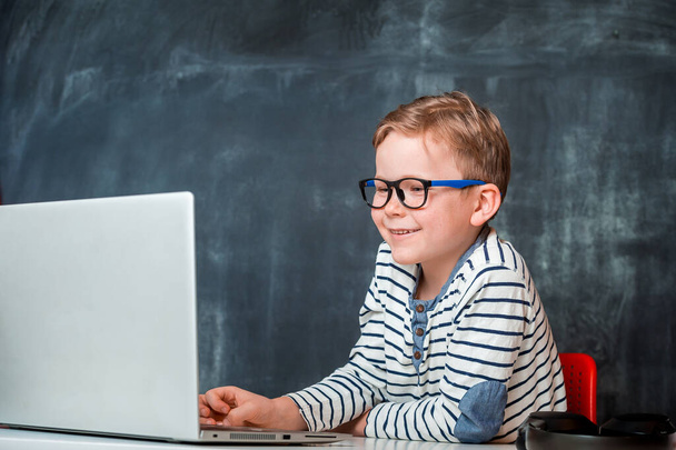 Portrait of boy in glasses playing video games. Kid has video call on laptop using zoom online virtual class , social distancing ,homeschooling,learning remotely during covid coronavirus pandemic - Photo, Image
