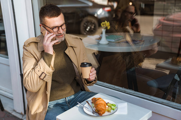 Confident businessman sitting at table in cafe using mobile phone - Foto, Bild