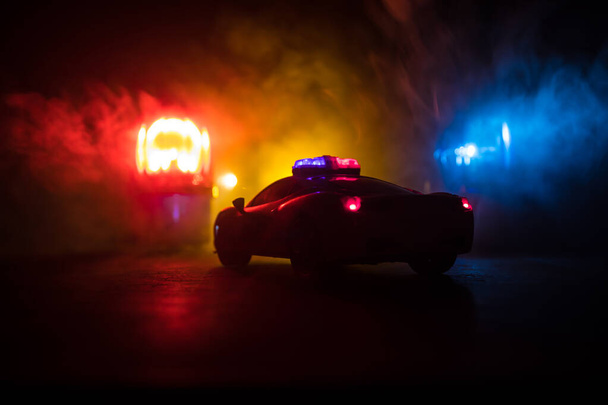 Radiowóz ściga samochód w nocy z mgłą w tle. Policyjny radiowóz ratowniczy jedzie na miejsce zbrodni. Kreatywna dekoracja. Skupienie selektywne - Zdjęcie, obraz