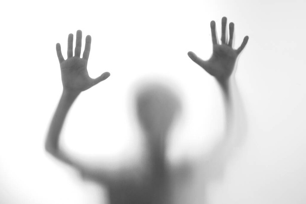 Silhouette scared boy stand behind glass door. Kid showing two hands. Background representing dangerous, fear, help, haunting, horror and panic. Teen problems, negative emotions concept. - Photo, Image