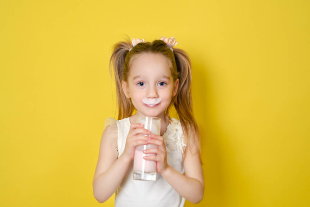 Kleines Mädchen trinkt Joghurt aus einem Glas auf gelbem Hintergrund. Konzept der gesunden Ernährung. - Foto, Bild