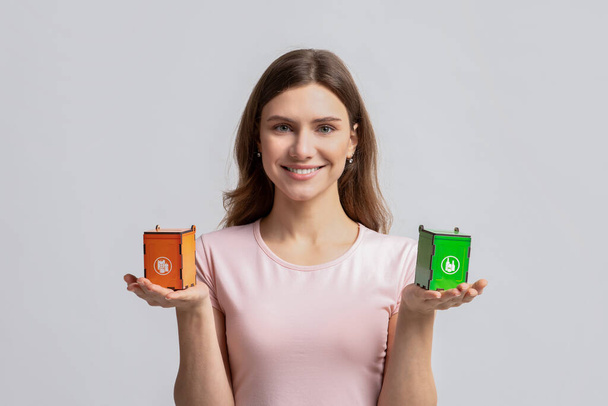 Mujer sonriente sosteniendo pequeñas papeleras de reciclaje de juguetes para diferentes tipos de residuos - Foto, Imagen