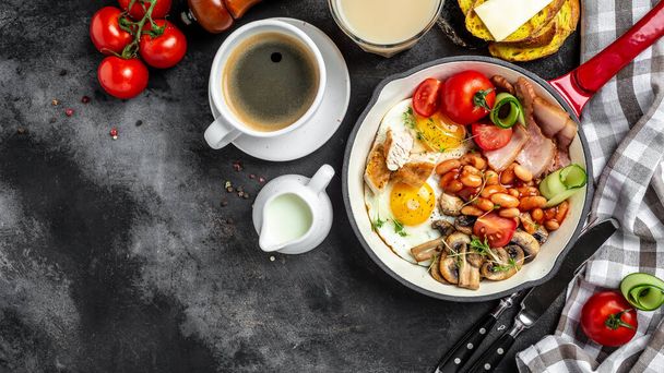 Englisches Frühstück in der Pfanne mit Spiegelei, Bohnen, Tomaten, Pilzen, Speck und Kaffee auf dunklem Hintergrund. Draufsicht mit Kopierraum, - Foto, Bild