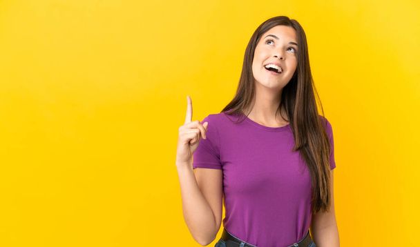 Teenager brasilianisches Mädchen über isoliertem gelben Hintergrund zeigt nach oben und überrascht - Foto, Bild