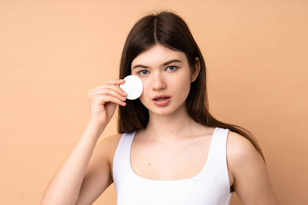 Young Ukrainian teenager girl over isolated background with cotton pad for removing makeup from her face - Photo, Image