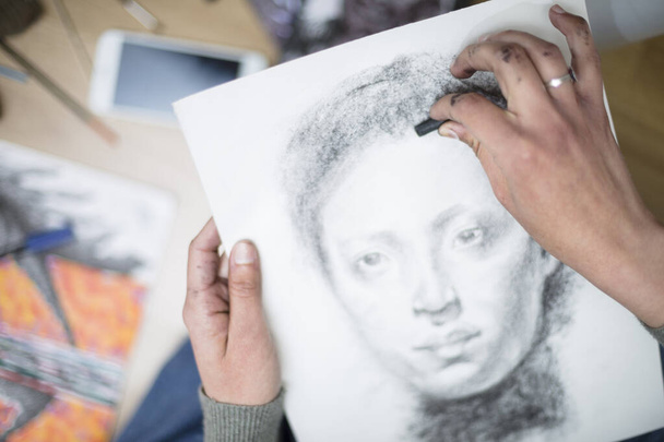 Bovenaanzicht van een close-up van de handen van een persoon die een portret in houtskool op een doek tekent. Concept van schilderlessen. Selectieve focus. Ruimte voor tekst. - Foto, afbeelding