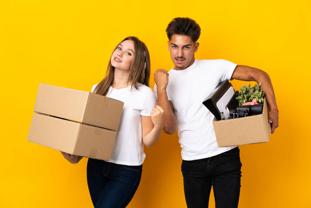 Teenager couple moving in new home among boxes isolated on blue background celebrating a victory - Photo, Image