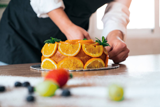 Jovem chef de pastelaria cozinhar um bolo de laranja com laranjas fatiadas - Foto, Imagem