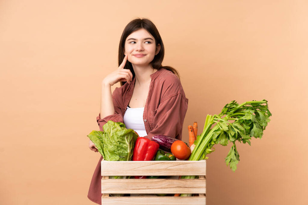 Jungbäuerin mit frisch gepflücktem Gemüse in einer Schachtel denkt beim Nachschlagen eine Idee nach - Foto, Bild