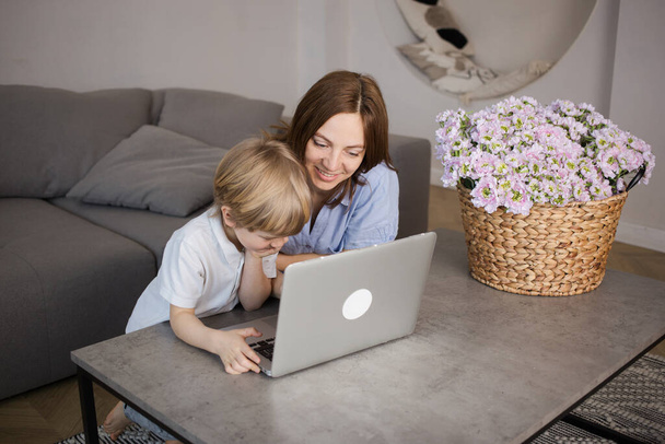 Pysy kotona. äiti ja poika kannettavalla tietokoneella, verkkokoulutus, auttaa lasta hallitsemaan nykyaikaista digitaalitekniikkaa. Mielenkiintoinen harrastus kotona sulkemisen aikana. Verkkoviestintä sukulaisten kanssa - Valokuva, kuva
