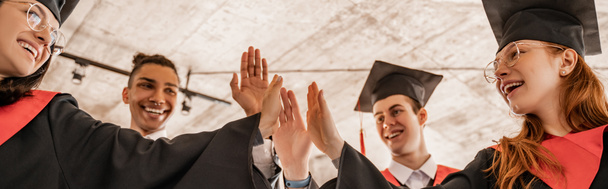 feliz interracial estudiantes en batas y gorras celebración diploma y dando alta cinco, graduación clase 2021, bandera - Foto, Imagen