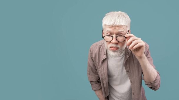 Problemas de visión. Joven chico albino en anteojos entrecerrados, fondo azul, panorama con espacio libre - Foto, Imagen