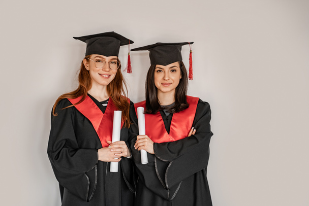 bonitos estudiantes en batas de graduación y gorras con diploma de rollos de papel, senior 2021 - Foto, Imagen
