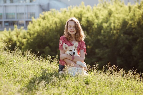 Cute teenager girl hugs welsh corgi pembroke dog outdoors in the city park in summer.  - Zdjęcie, obraz