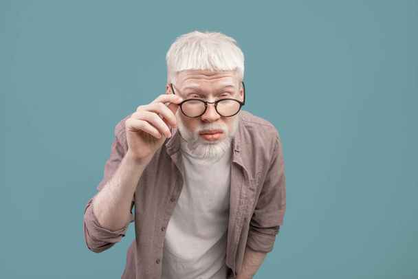 Poor eyesight. Albino man in eyeglasses squinting eyes, having bad sight, trying to see something over blue background - Photo, Image