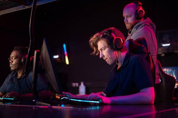 Durante o torneio Dota 2, dois caras da equipe jogam nos computadores, o treinador observa por trás - Foto, Imagem