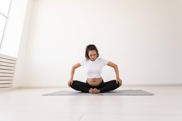 Σκοπίμως έγκυος γυναίκα γυμνάζεται κατά τη διάρκεια του μαθήματος γιόγκα και χαλαρώνει ενώ κάθεται σε ένα χαλάκι στο πάτωμα. Έννοια της σωματικής και ψυχικής προετοιμασίας του σώματος για τον τοκετό. Θέση για κείμενο - Φωτογραφία, εικόνα