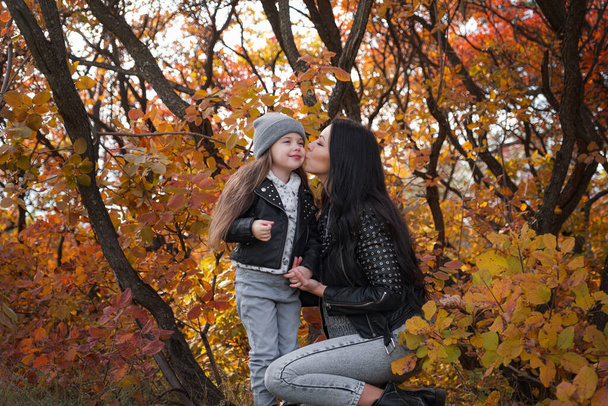 幸せな家族の母親と子供の娘が秋の散歩で遊んで笑っています。母親と子供の関係。ファッショナブルな母と娘でスタイリッシュな外観で同じ革のジャケットとセーター - 写真・画像