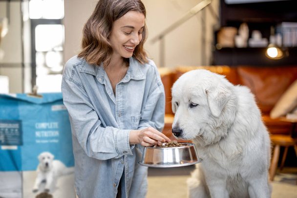 Mujer alimenta a un perro con comida seca en casa - Foto, Imagen