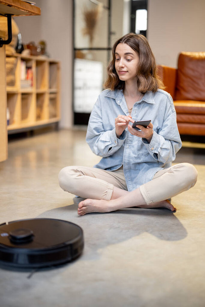 Relaxed woman with phone and robotic vacuum cleaner - Photo, Image